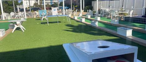 An outdoor area with artificial grass, white tables, and chairs, and a covered seating area with umbrellas.
