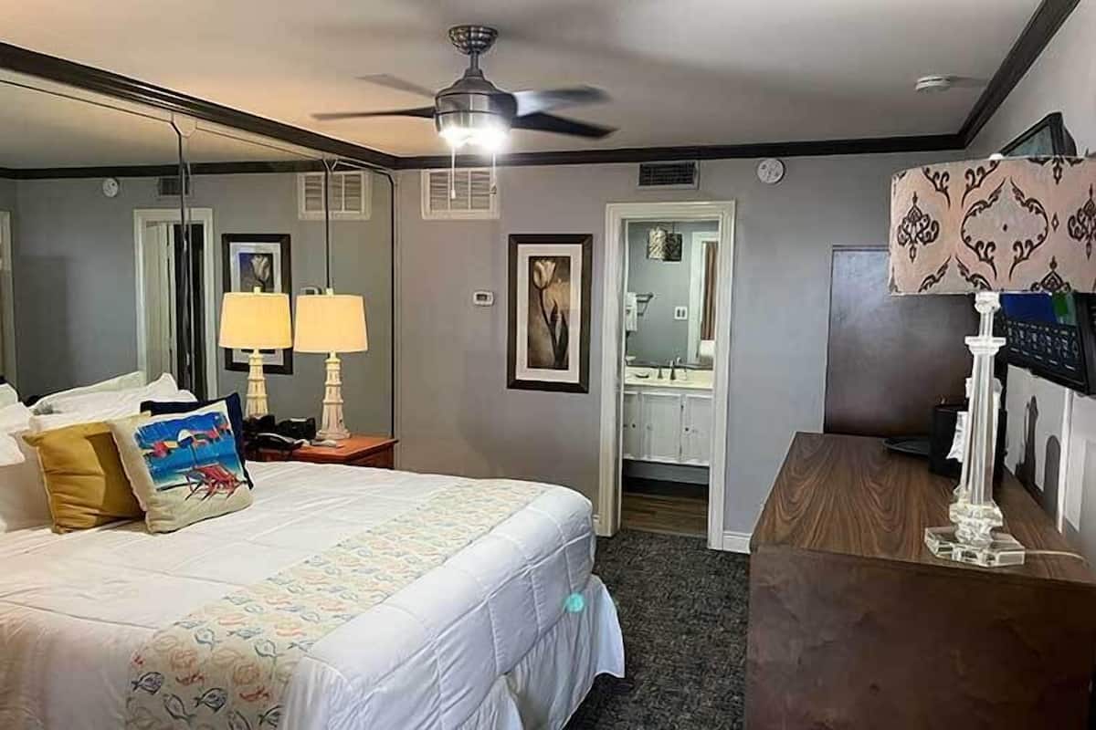 A hotel room with a bed, bedside lamps, a desk, a mirror, and a ceiling fan.