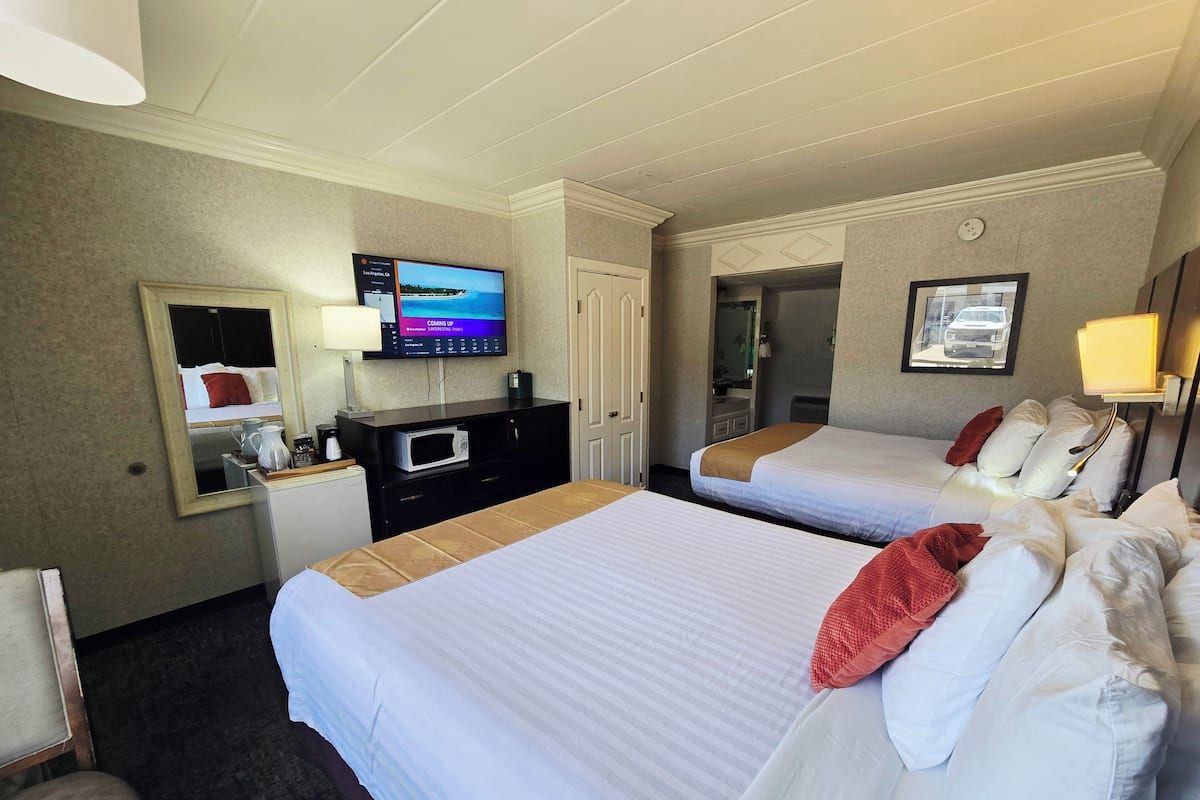 A hotel room with two beds, a television, a desk with a microwave, and a mirror.