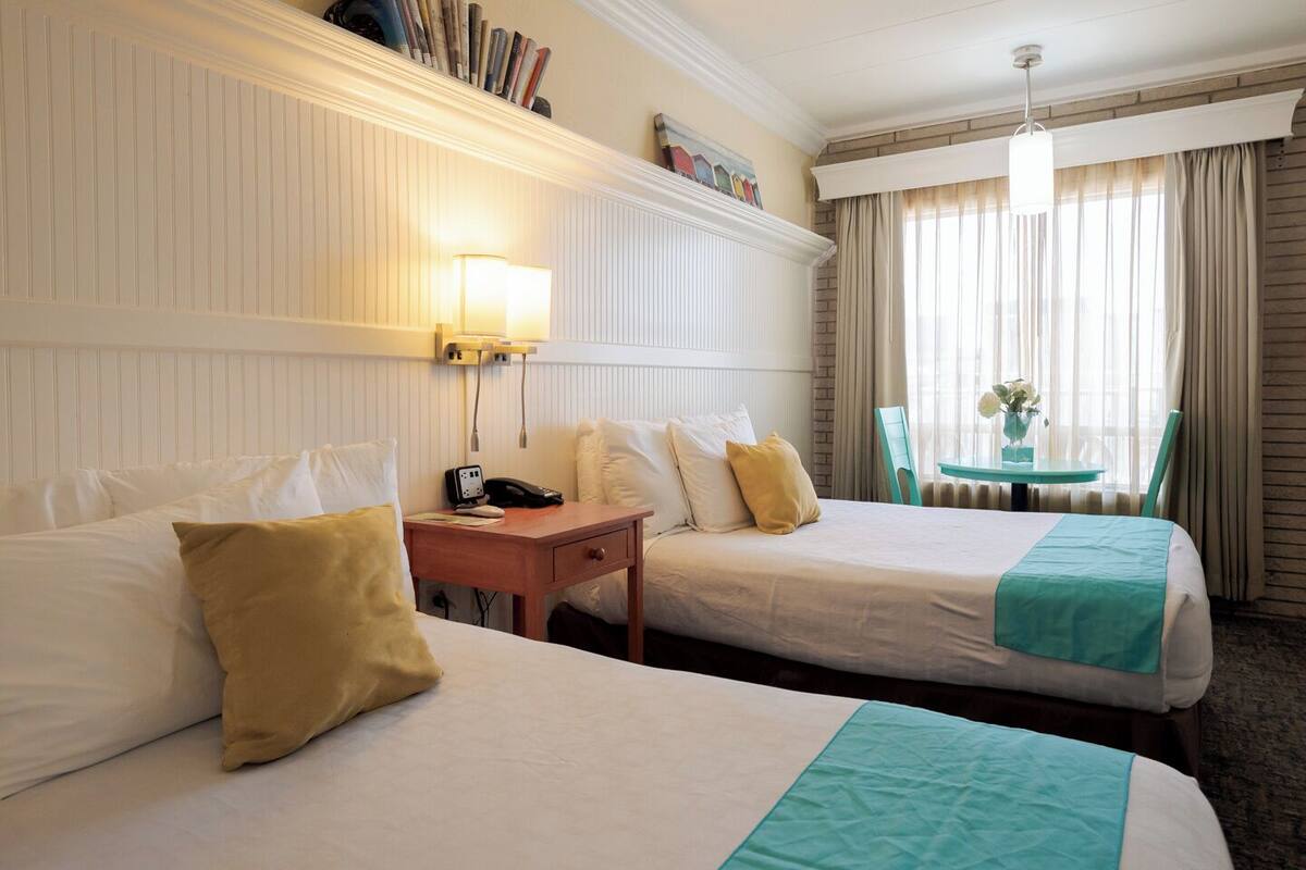 A hotel room with two beds, a desk, a telephone, and a window with curtains.
