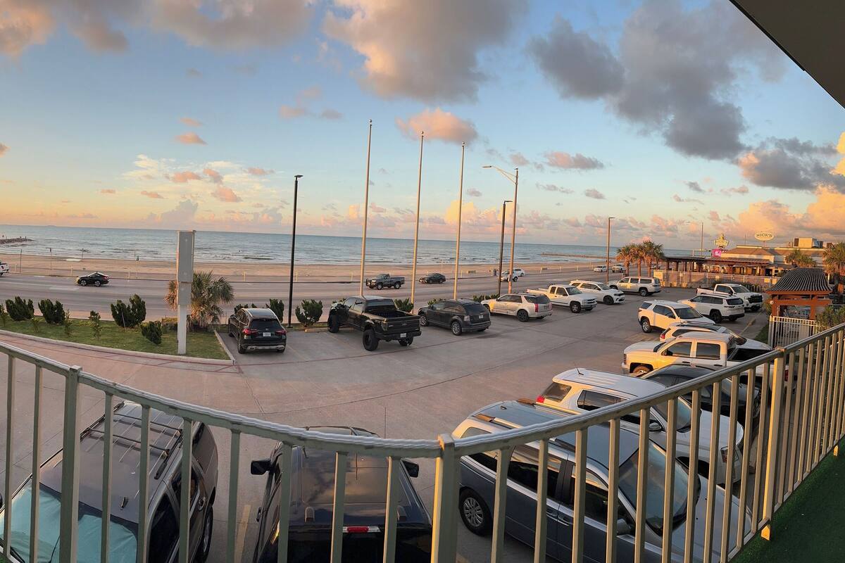 A view from a balcony overlooking a parking lot with a beach and ocean in the background.