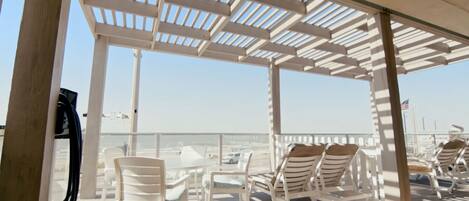 A covered outdoor area with white chairs and tables, overlooking a beach.