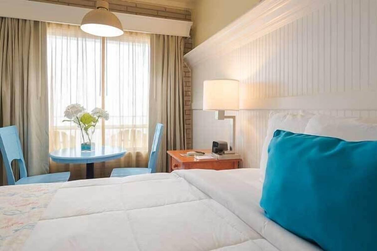 A hotel room with a bed, a table, chairs, a lamp, and a window with curtains.