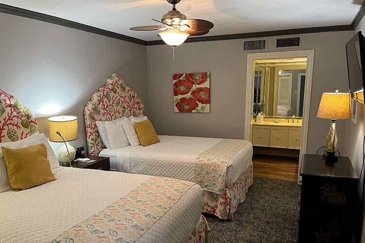 A hotel room with two beds, a ceiling fan, a mirror, a lamp, and a dresser.