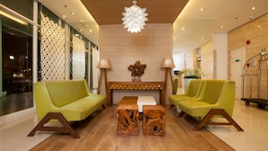 Un vestíbulo con dos sofás verdes, una mesa de centro de madera y un elemento decorativo en la pared.