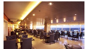 A spacious hotel lobby with multiple seating areas, a bar, and large windows offering a city view.