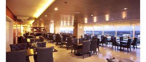 A spacious hotel lobby with multiple seating areas, a bar, and large windows offering a city view.