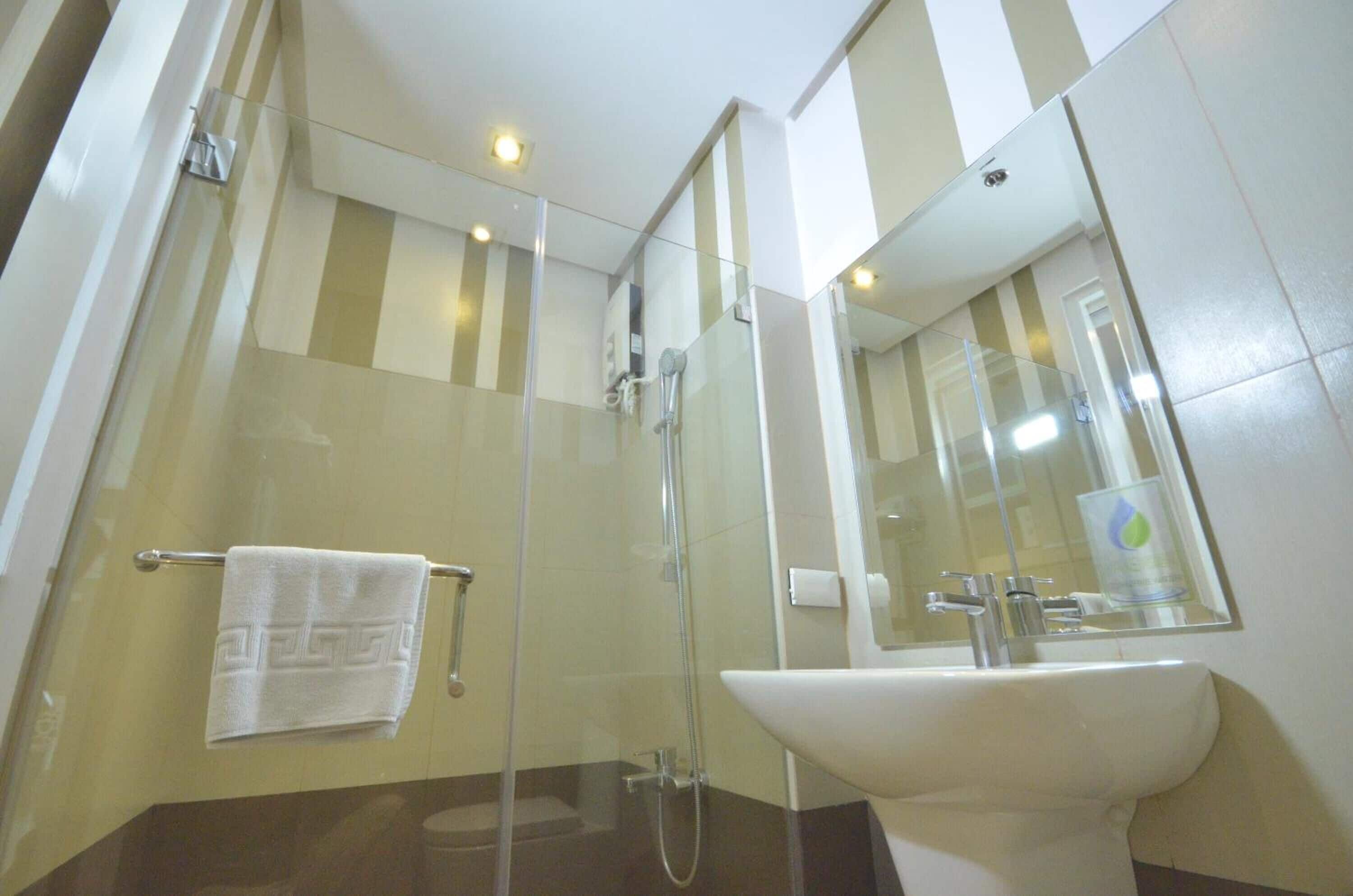 Un baño moderno con ducha acristalada, lavamanos blanco y un espejo grande.