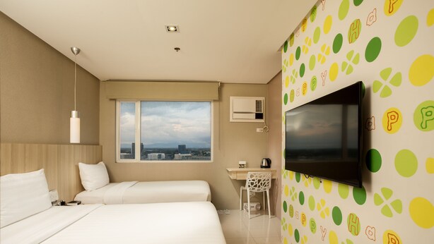 A hotel room with two beds, a desk, a TV, and a window with a city view.