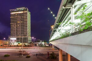 Un immeuble de grande hauteur, avec de nombreux étages, une passerelle piétonne et une grue de construction en arrière-plan.