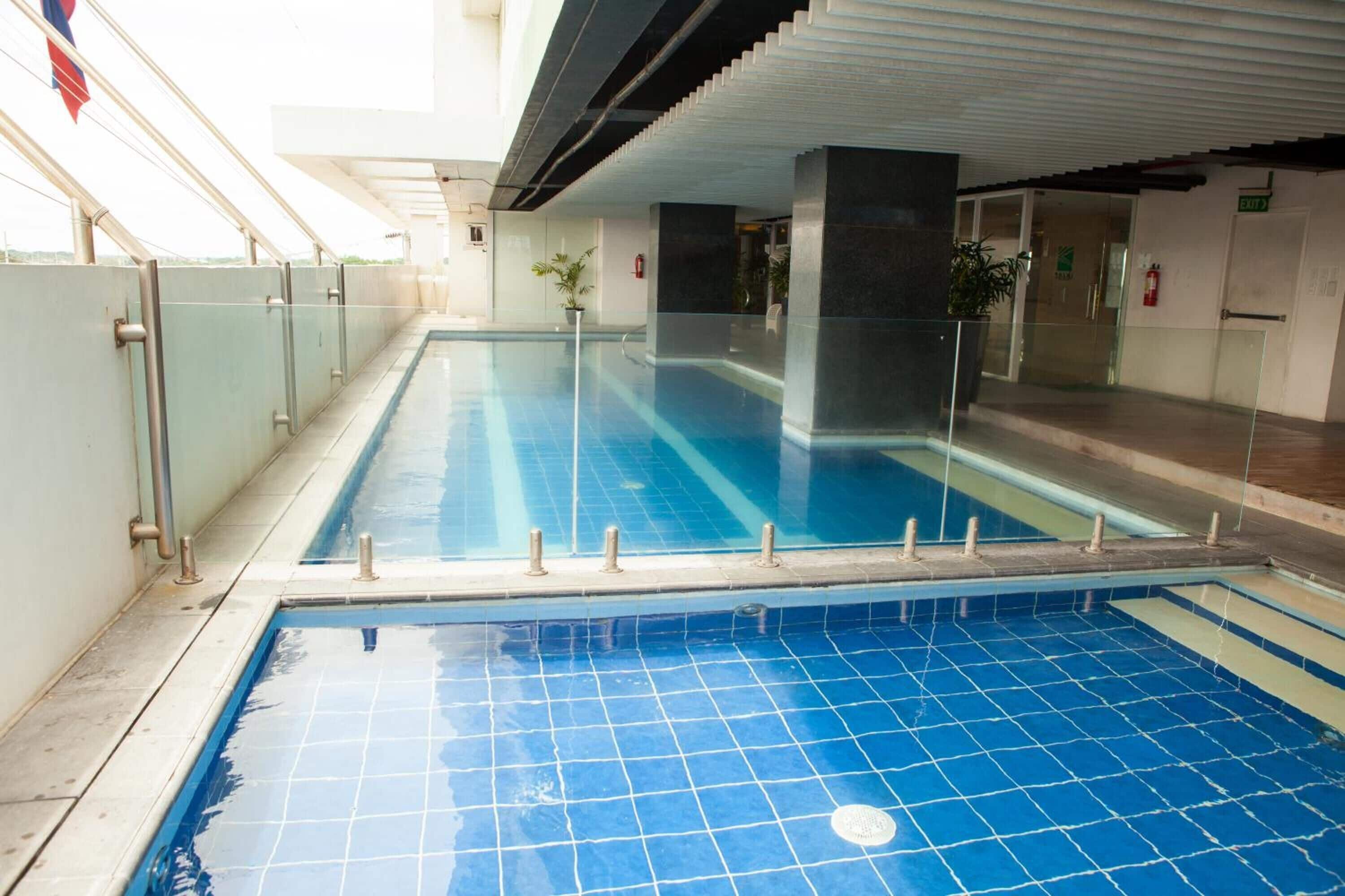 An indoor swimming pool with clear water, surrounded by glass railings and a tiled floor.