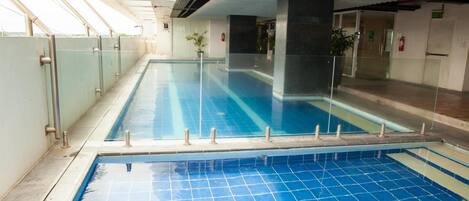 Una piscina interior con agua cristalina, rodeada de barandillas de vidrio y un suelo de baldosas.