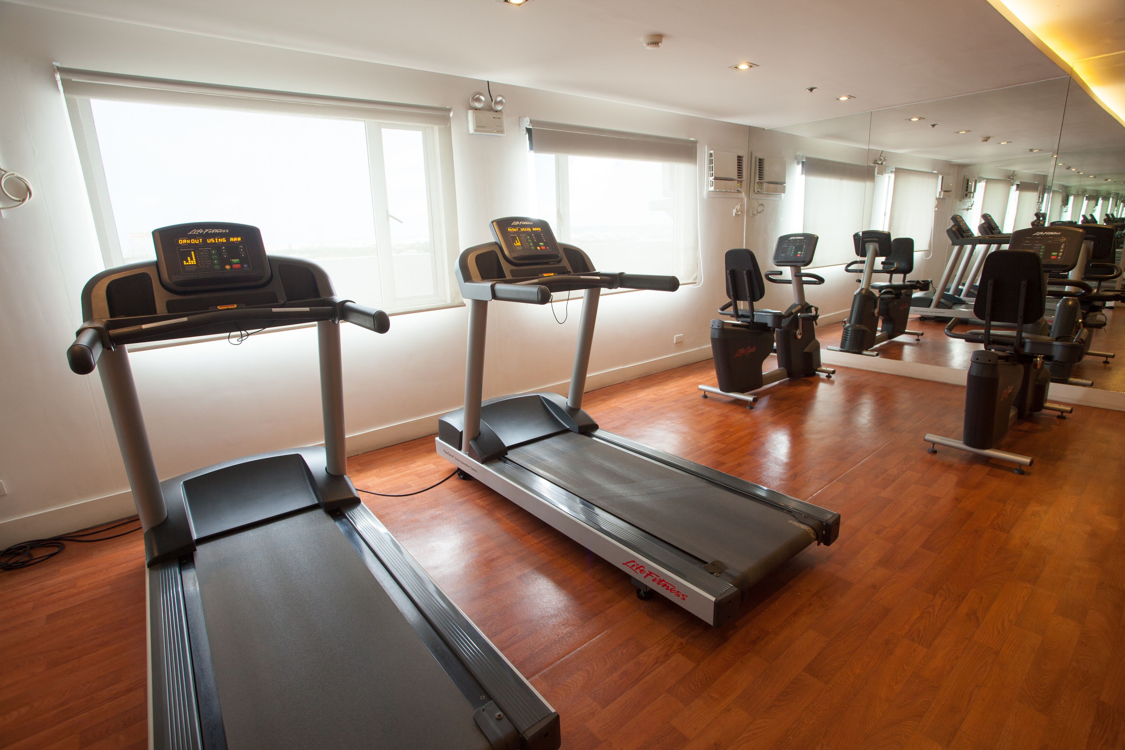 A gym with treadmills, exercise bikes, and a mirrored wall.