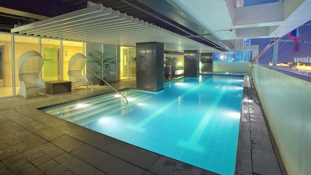 Piscina interior moderna con agua azul cristalina, rodeada de sillones de descanso y plantas en macetas.