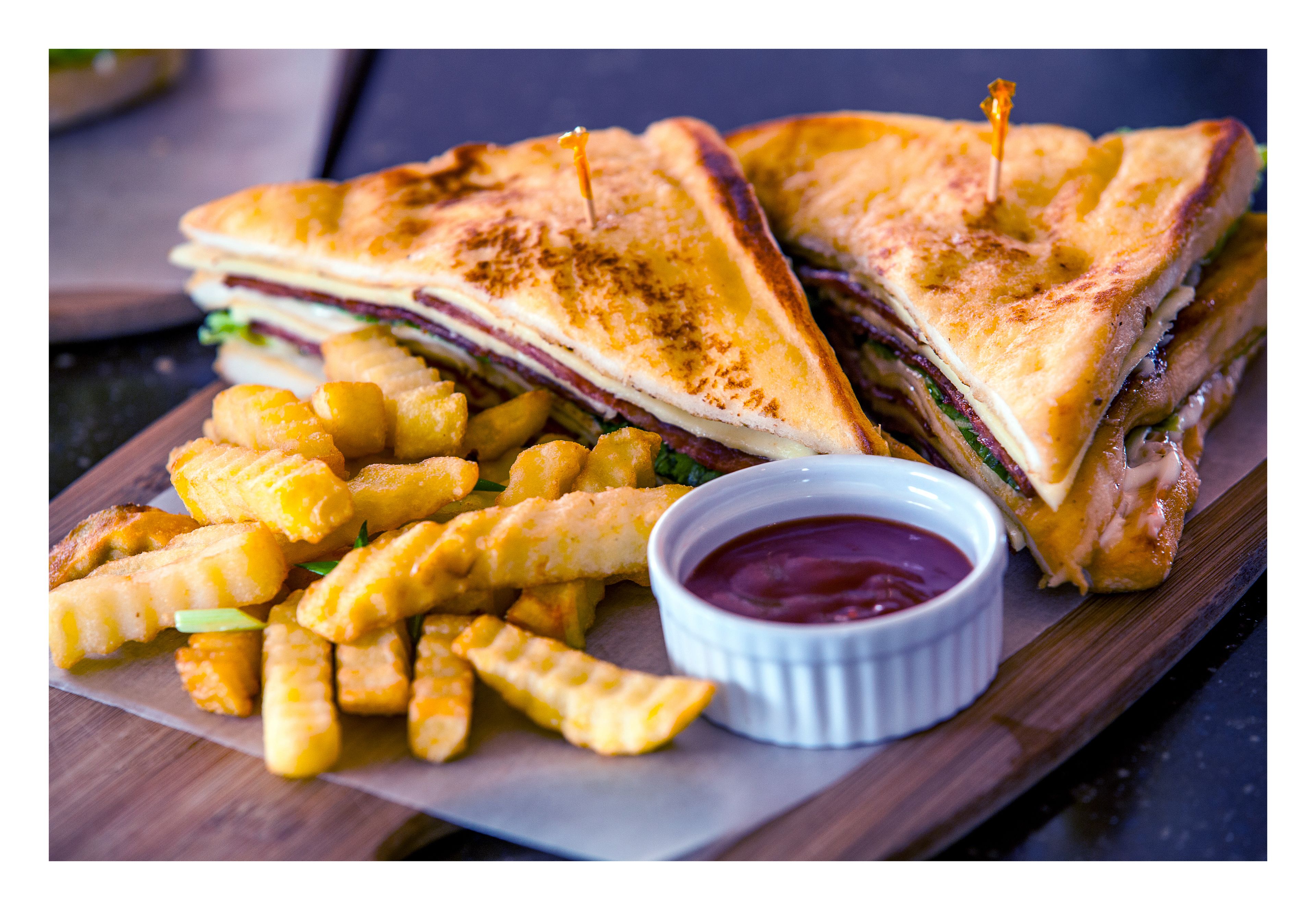A grilled sandwich with fries and ketchup on a wooden board.
