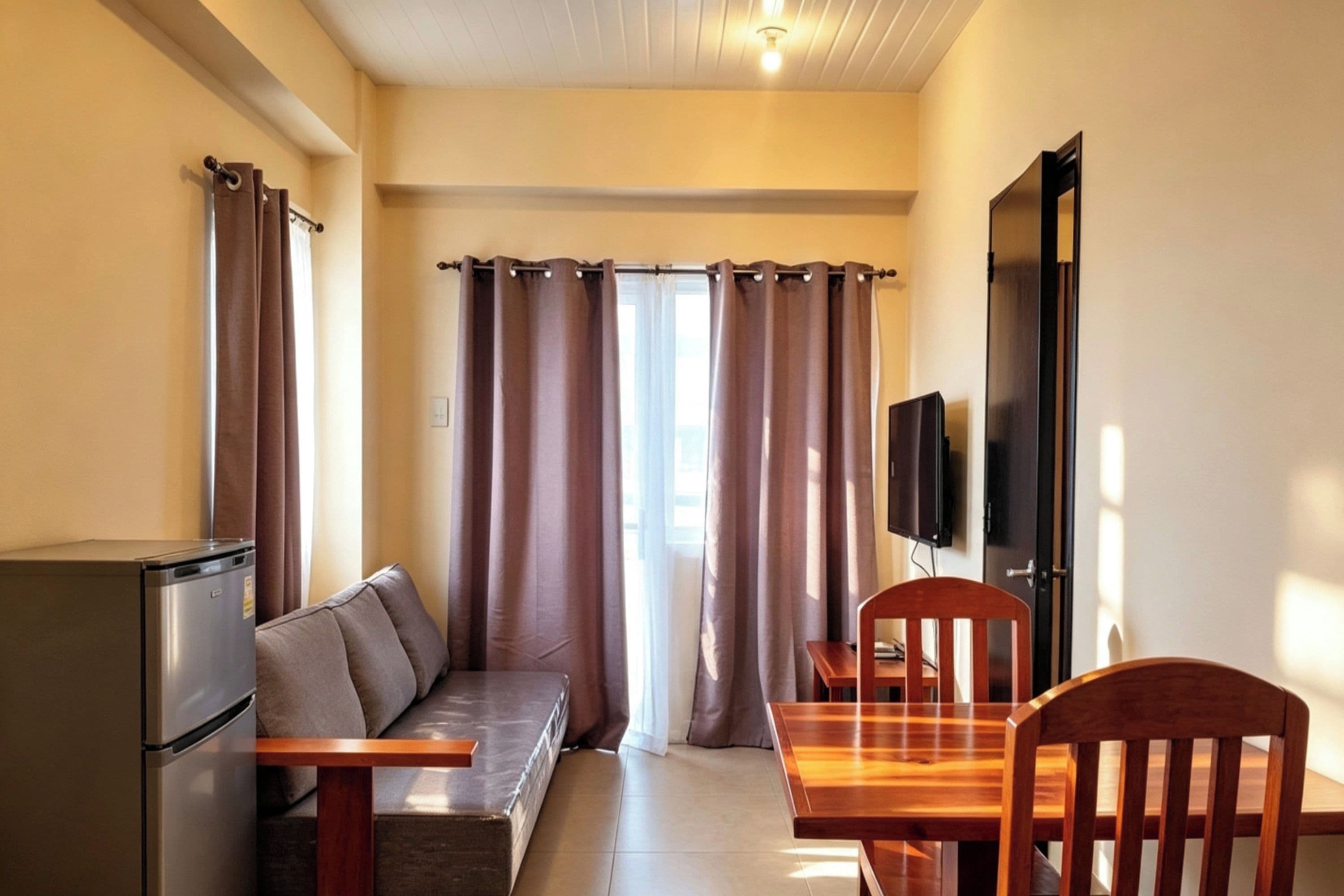 A compact living space with a kitchenette, a sofa, a dining table with chairs, and a television mounted on the wall.
