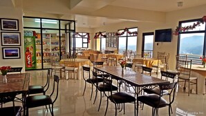 A dining area with tables and chairs, a buffet with food items, and a view of the mountains through large windows. - Gardenville Hotel (Baguio)