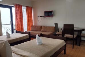 A hotel room with a sofa, two beds, a TV, a table, and a chair. - Gardenville Hotel (Baguio)