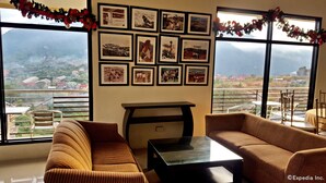 A room with a sofa, a coffee table, and a wall decorated with framed photographs. - Gardenville Hotel (Baguio)