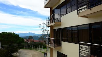 A multi-story building with balconies, large windows, and a view of a mountainous landscape.