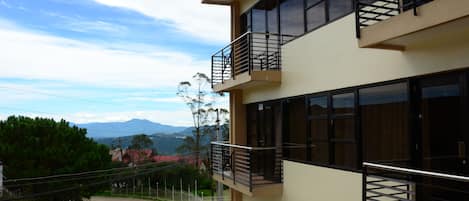 Un edificio de varios pisos con balcones, ventanas amplias y vistas a un paisaje montañoso.