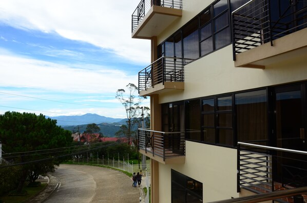 Un edificio de varios pisos con balcones, ventanas amplias y vistas a un paisaje montañoso.
