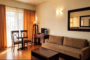 A hotel room with a sofa, a desk, two chairs, a lamp, and a large mirror on the wall. - Gardenville Hotel (Baguio)