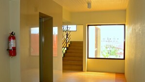 A hallway with a fire extinguisher, a staircase, and a large window with a view of buildings. - Gardenville Hotel (Baguio)