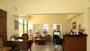 A reception area with a reception desk, seating area with sofas and chairs, a coffee table, and a large window with blinds. - Gardenville Hotel (Baguio)