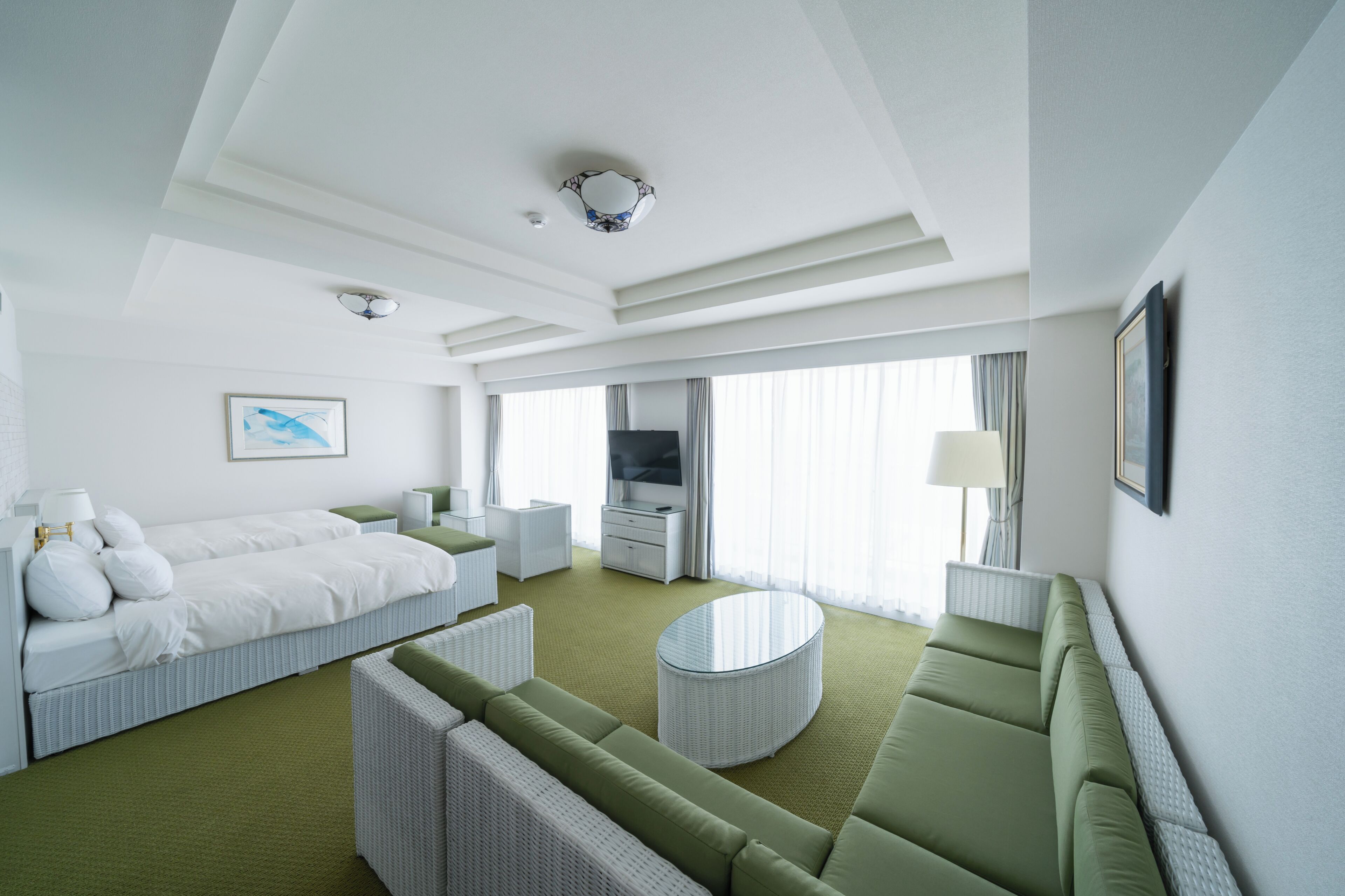 Une chambre d’hôtel avec un lit, un canapé vert, une table basse ronde, une télévision et un tableau au mur.