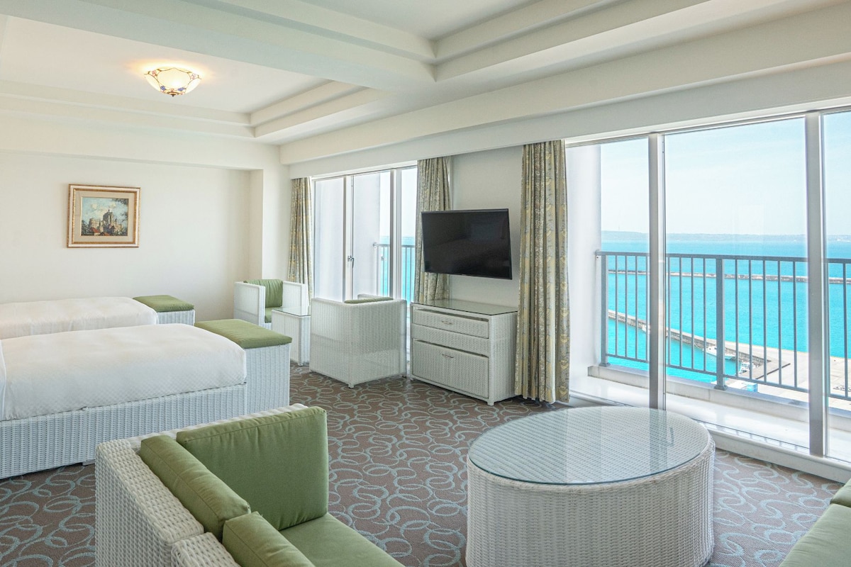 A hotel room with a bed, seating area, TV, and a balcony with a view.