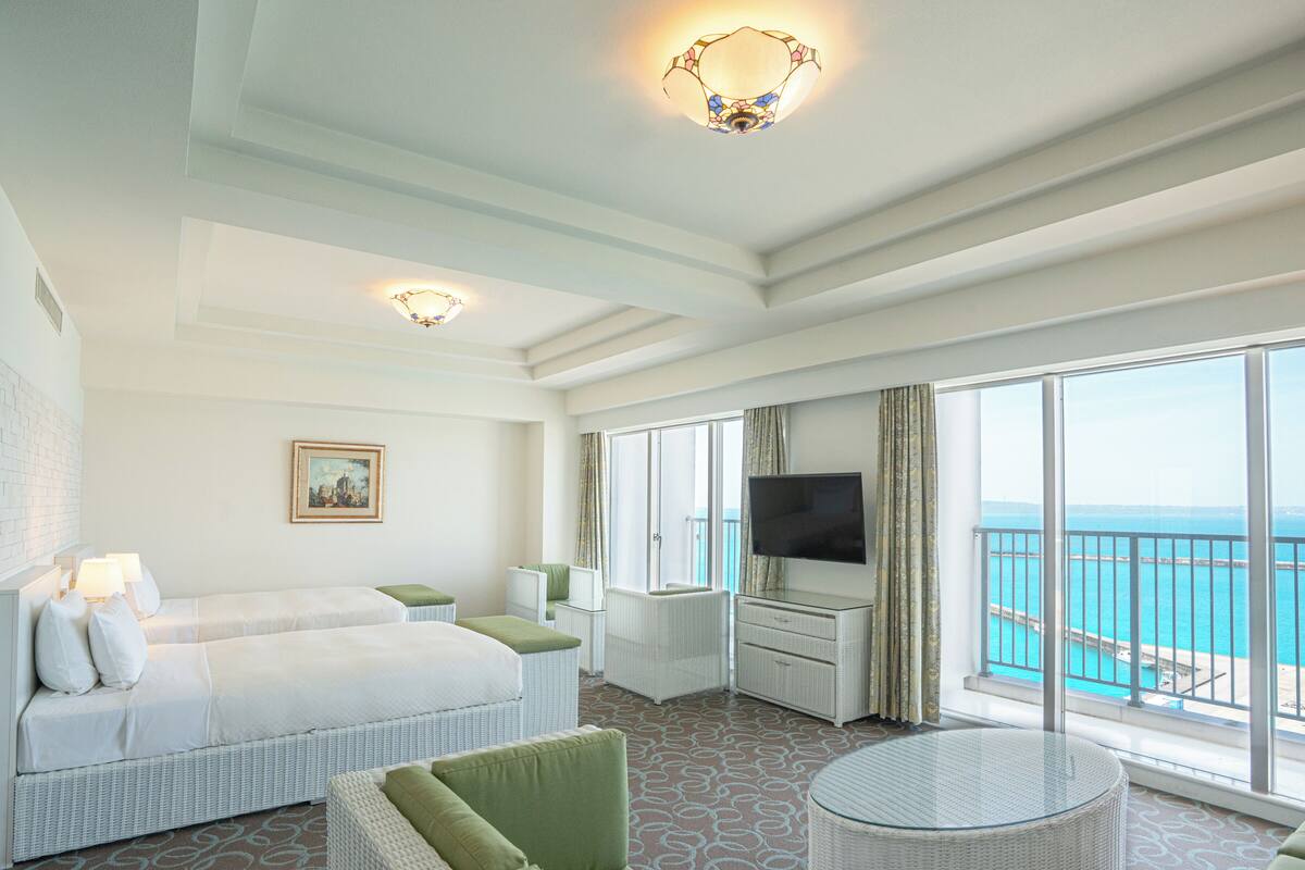 Une chambre d’hôtel avec un grand lit, un canapé, une télévision et un balcon donnant sur la mer.