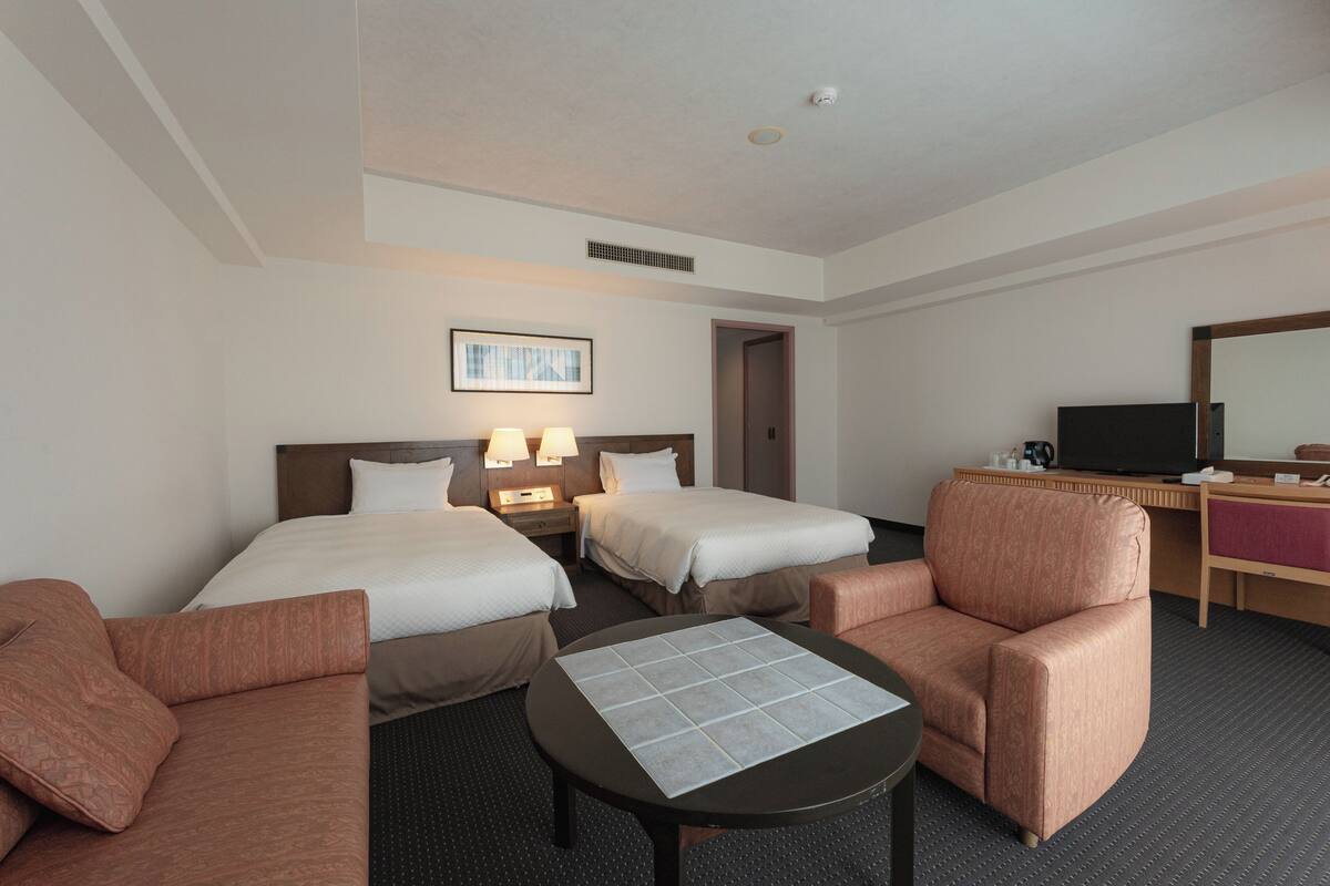 Une chambre d’hôtel avec deux lits, un bureau, une chaise, une télévision et une petite table.
