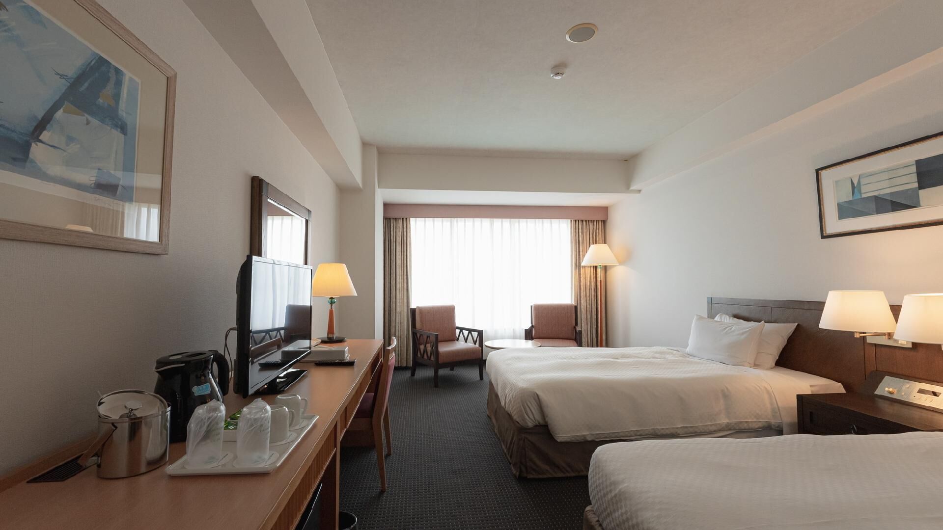 Une chambre d’hôtel avec un lit, un bureau avec une télévision, une chaise et une fenêtre avec des rideaux.