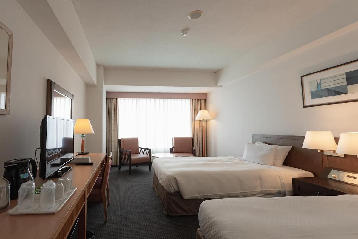 A hotel room with a bed, a desk with a television, a chair, and a window with curtains.