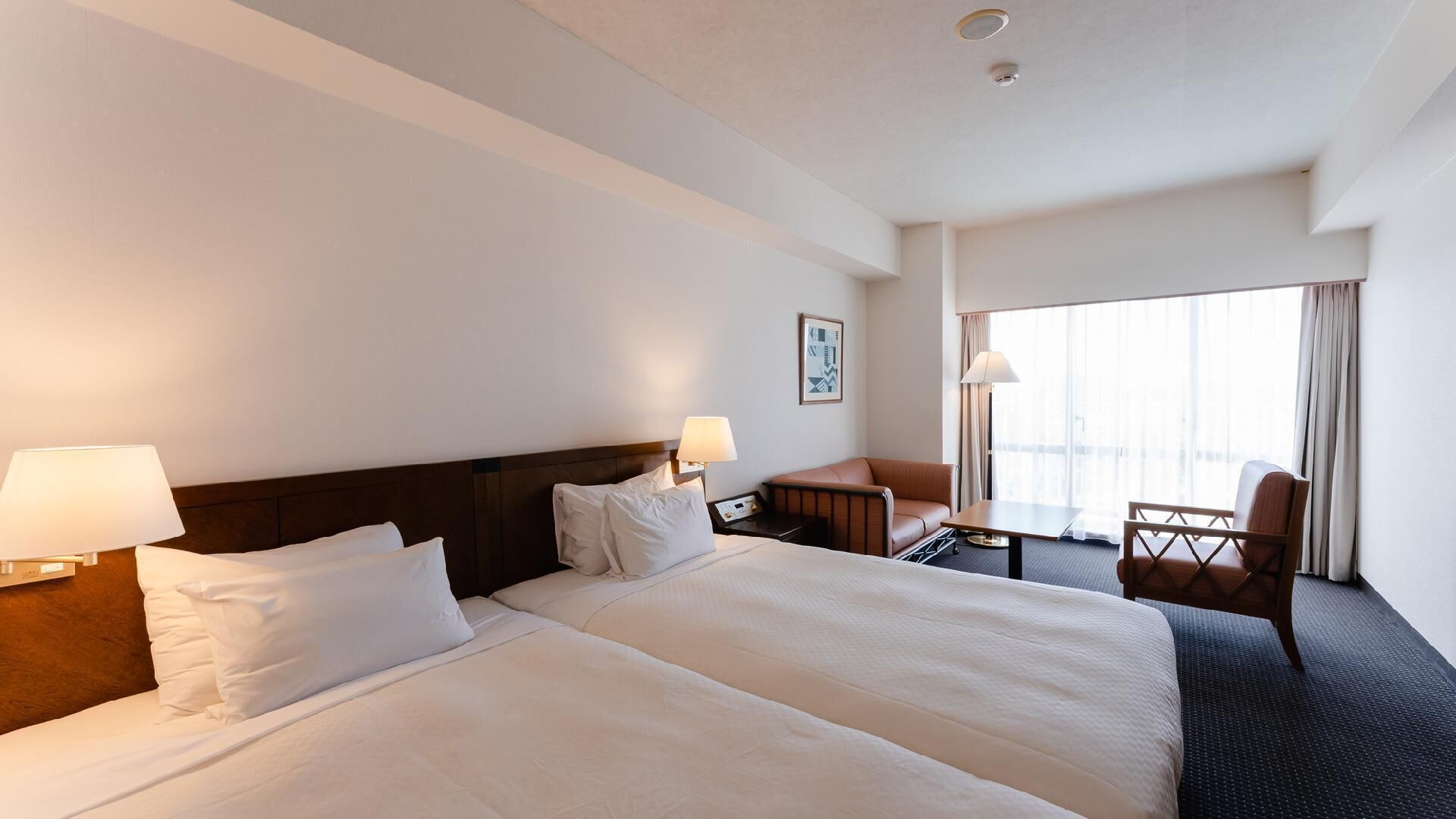 Une chambre d’hôtel avec deux lits, un bureau, une chaise et une grande fenêtre.