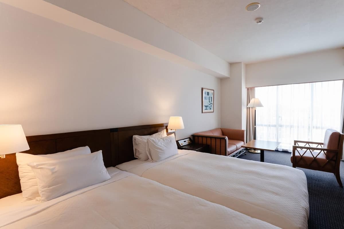 A hotel room with two beds, a desk, a chair, and a large window.