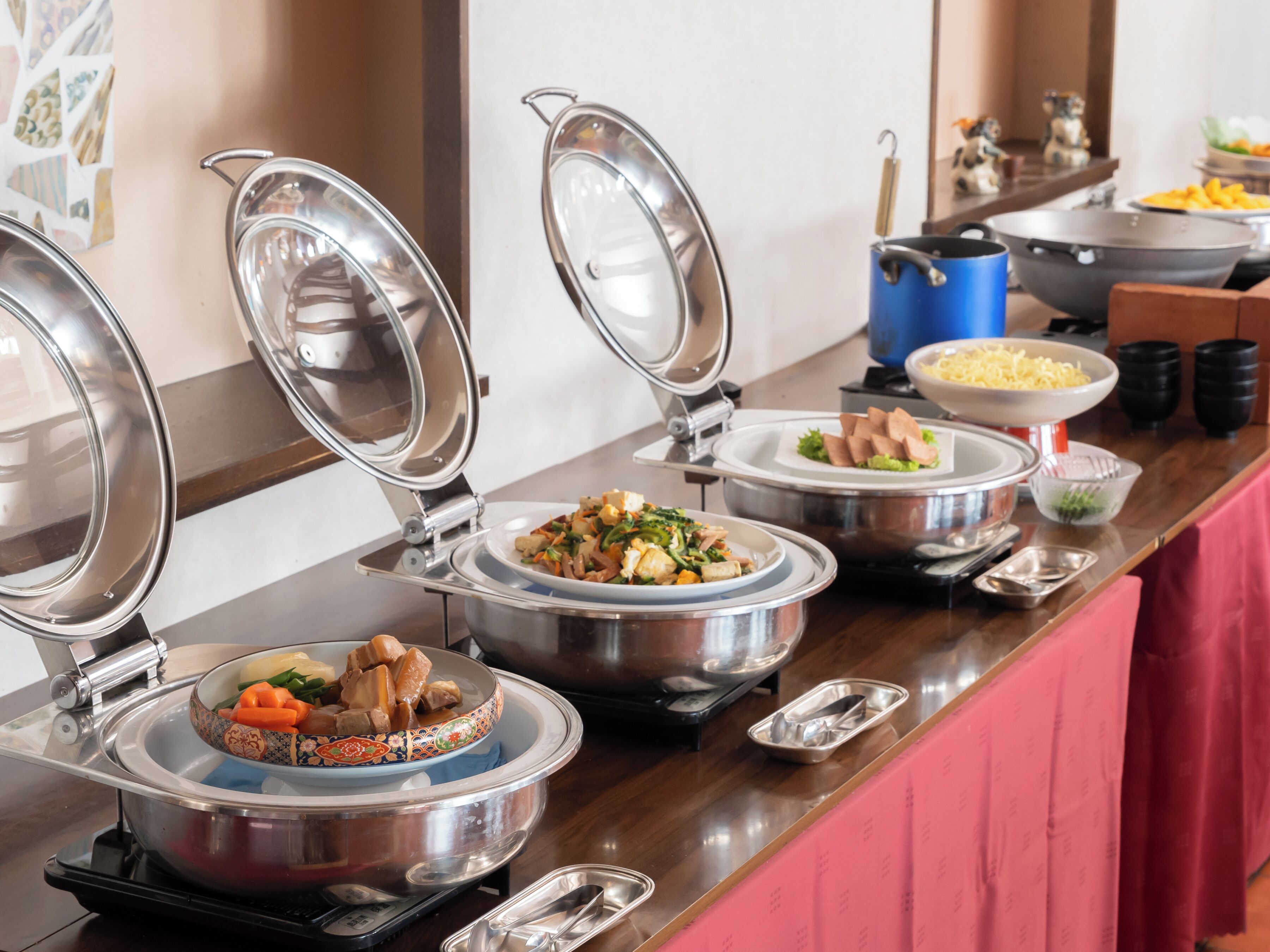A buffet setup with multiple covered dishes, including a variety of foods and a blue pot.