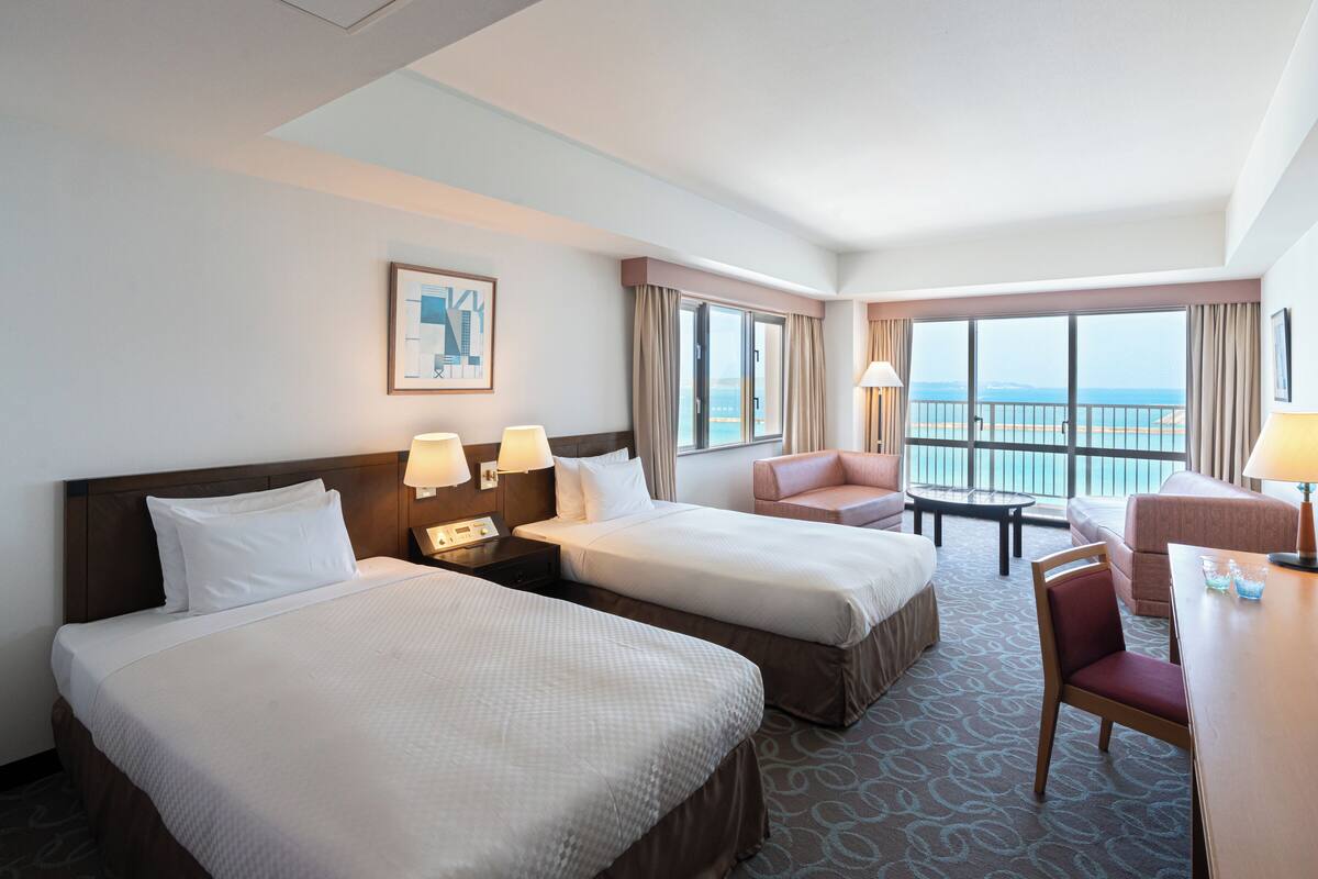 Une chambre d’hôtel avec deux lits, un bureau, une chaise et une vue sur la mer.