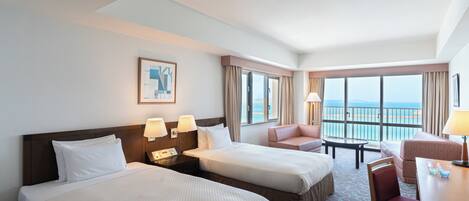 Ein Hotelzimmer mit zwei Betten, einem Schreibtisch, einem Stuhl und Meerblick.