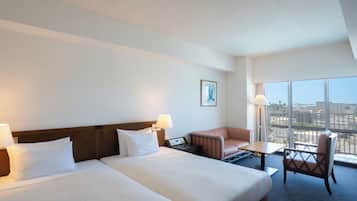 Habitación de hotel con dos camas, un escritorio, una silla y un ventanal con vistas a la ciudad.
