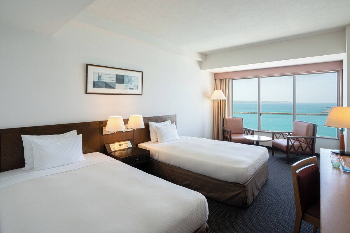 Une chambre d’hôtel avec deux lits, un bureau et une vue sur la mer.