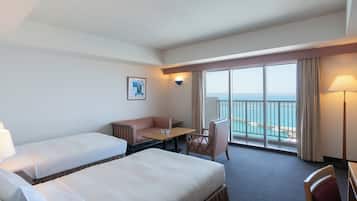 Habitación de hotel con dos camas, un escritorio, una silla, vista al mar y un cuadro en la pared.