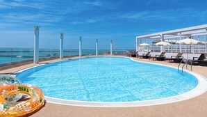 Ein Poolbereich mit klarem, blauem Wasser, Liegestühlen und Sonnenschirmen.
