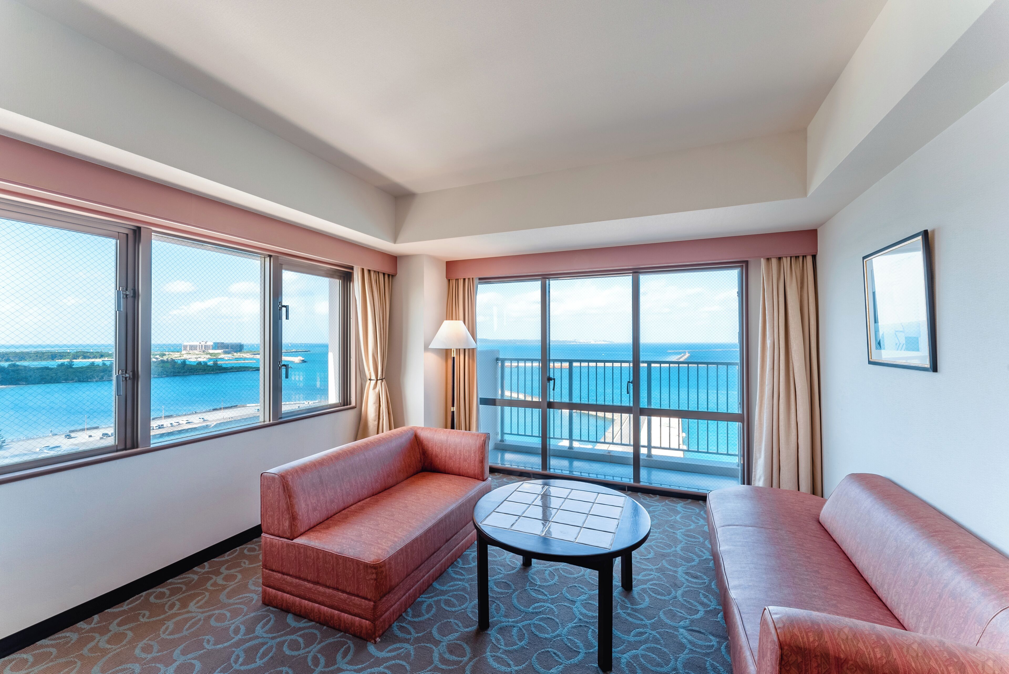 Une chambre d’hôtel avec un balcon, un canapé, une table et une vue sur la mer.
