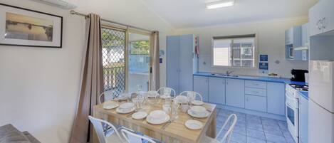 Una cocina limpia y moderna con armarios blancos y una zona de comedor con una mesa dispuesta para cuatro comensales.