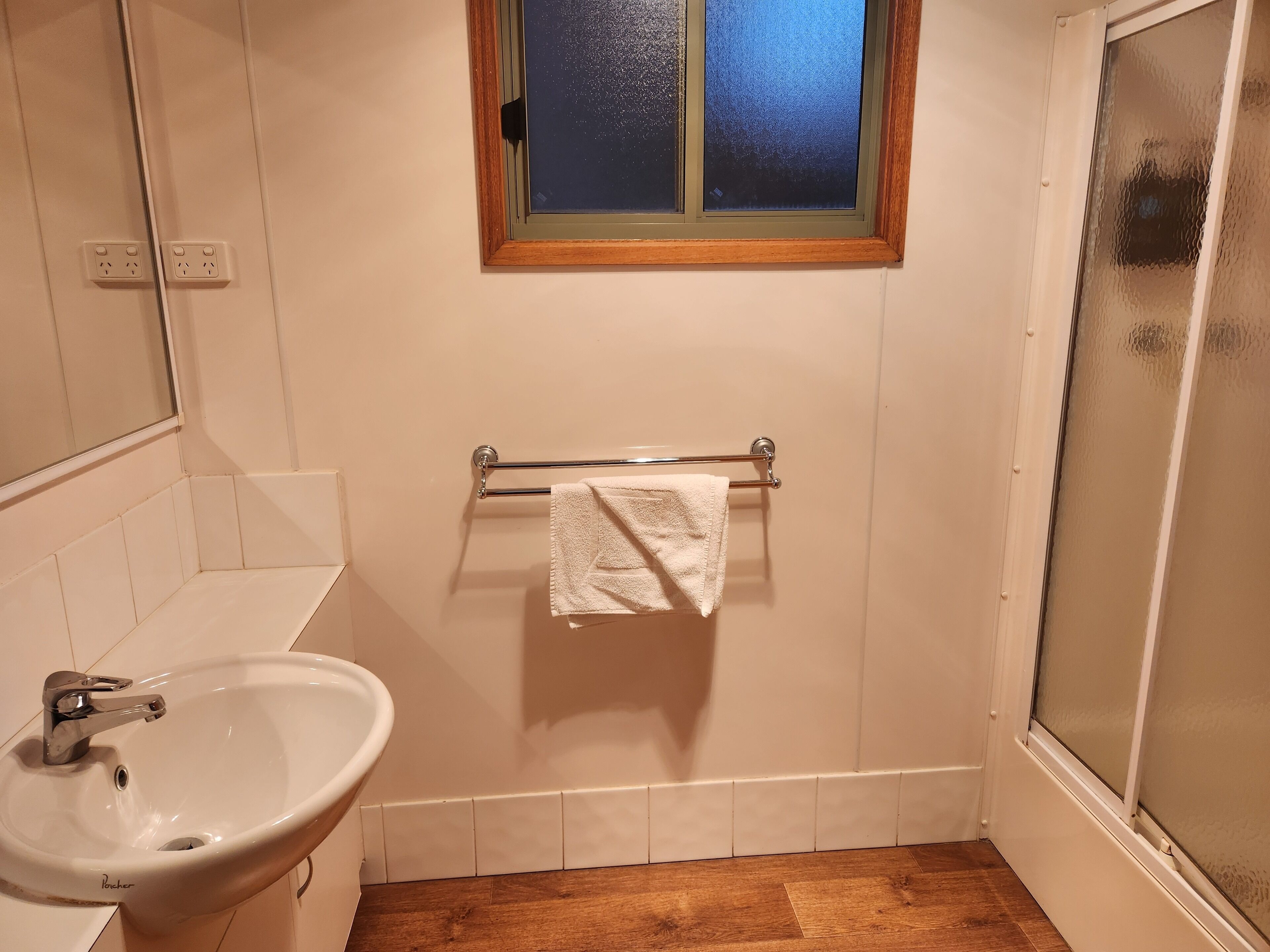 A bathroom with a sink, a towel rack with a towel, a window, and a shower area.