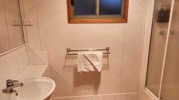 A bathroom with a sink, a towel rack with a towel, a window, and a shower area.