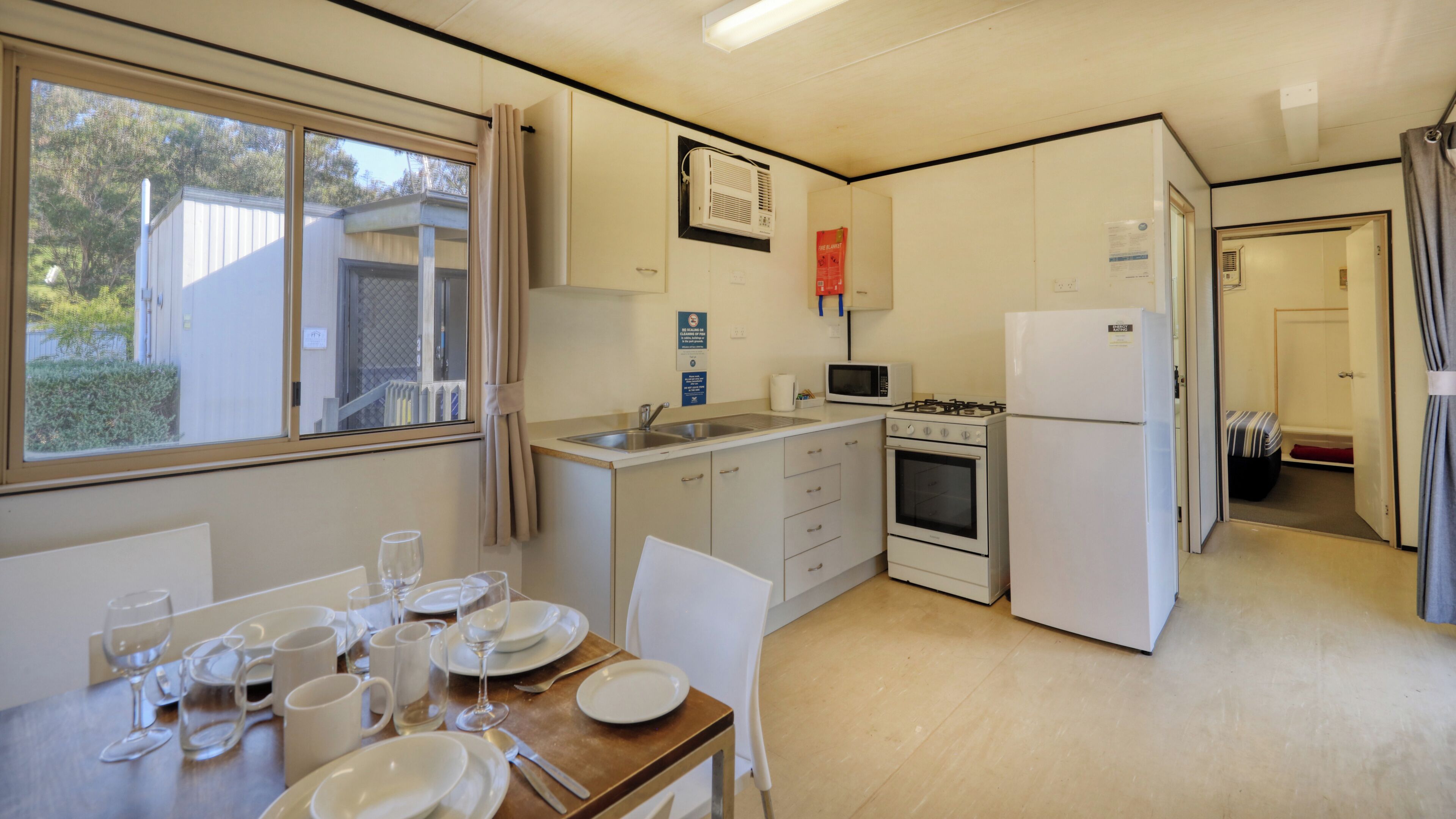 A compact kitchen with a sink, stove, and microwave. There is a dining area with a table set for two.