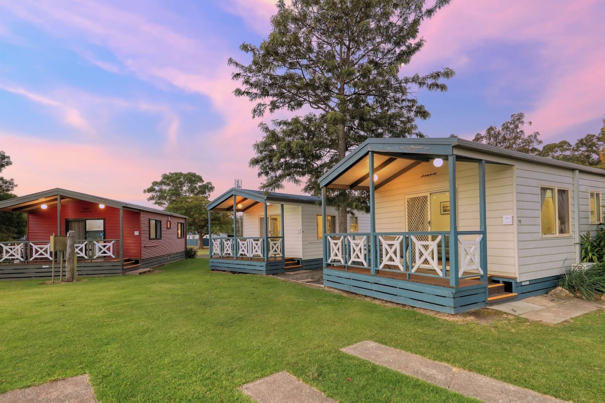 A row of mobile homes with a grassy lawn and trees in the background.